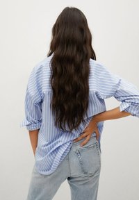 Blue and white striped button-up shirt with rolled sleeves, relaxed fit, worn with light blue denim jeans, displaying textured fabric.