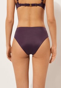 Högmidjad bikiniunderdel i mörklila tyg, slät textur, minimalistisk design utan synliga mönster eller detaljer.