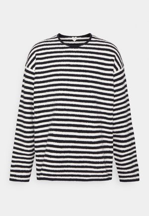 Musta-valkoisessa raidallisessa pitkähihnaisessa poolo-paidassa on pehmeä, teksturoitu kangas. Pyöreä kaula-aukko ja väljä istuvuus. Vaakasuorat raidat vaihtelevat leveydeltään.