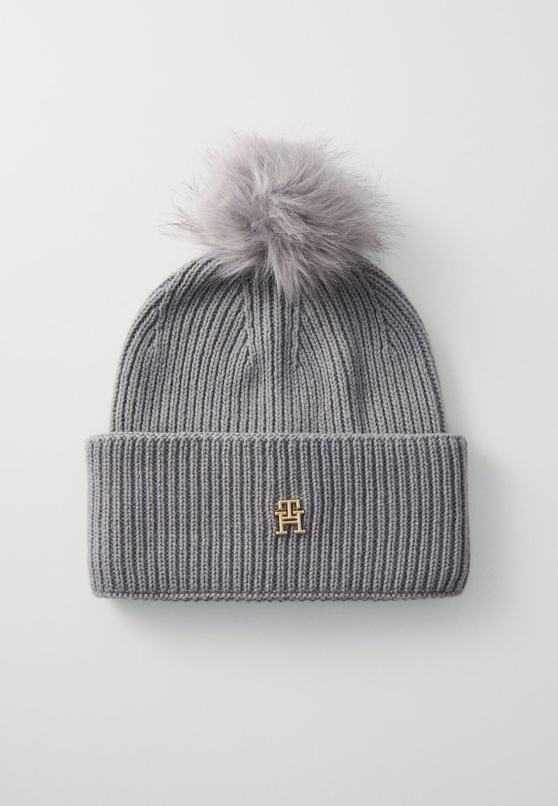 Bonnet en tricot gris avec un revers, surmonté d'un pompon gris duveteux, arborant un petit logo doré à l'avant.