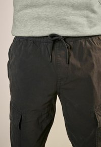 Schwarze Cargo-Hose mit verstellbarem Kordelzug, ausgestattet mit Seitentaschen und einem strukturierten Gewebe. Minimalistisches Design, funktional und lässig.
