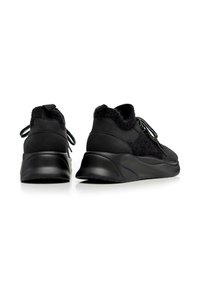 Zapatillas negras con un upper texturizado, que presenta una combinación de materiales suaves y aterciopelados. El diseño incluye cordones y una suela gruesa para mayor soporte.