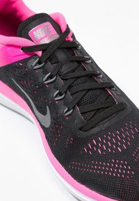 Scarpa da corsa Nike nera e rosa con tomaia in mesh traspirante, dettagli grigi e suola ammortizzata. Presenta una punta arrotondata e un design con lacci.