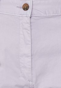 Tecido lilás claro com uma textura suave, apresentando um botão de metal e detalhes em costura visíveis na parte frontal da calça.