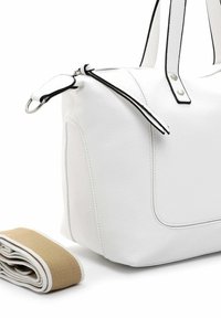 Hvid læderhåndtaske med sort kant og metallynlås, ledsaget af en rullet aftagelig beige og hvid stofrem på en hvid baggrund.