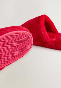 Rød faux fur tåbel med en tykk, struktureret sål, der har et bølget mønster. Oversiden dækker foden fuldt ud med blødt, plush materiale.