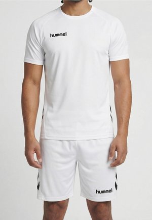 Mand iført hvid hummel sportstøj med korte ærmer og shorts, stående mod en ensfarvet lys baggrund.