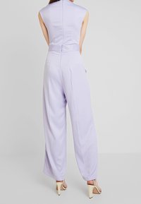 Lila jumpsuit med en figursydd överdel, ärmlös design, vida byxor och dragkedja bak. Slät textur och minimalistisk stil.