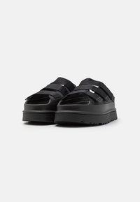 Scarpe platform nere con una texture liscia, caratterizzate da cinture larghe, una punta arrotondata e una suola spessa e gommata per una buona aderenza.