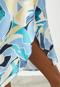 Kurzes, hellblaues Kleid mit abstrakten Mustern in verschiedenen Blautönen und Gelb. Hat einen seitlichen Schlitz und eine glatte Stofftextur.