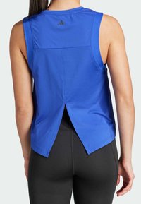 Blauwe atletische tanktop met een geribbelde textuur, mouwloos ontwerp en een gespleten detail aan de achterkant. Zwart logo-accent nabij de halslijn.