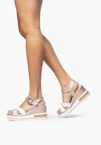 Wedge sandals featuring a white and beige color scheme, synthetic straps, and a buckle closure. Thick sole with textured detailing.