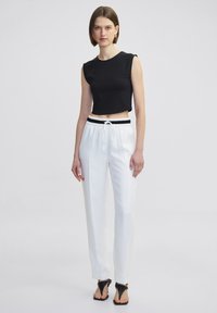 Zwarte cropped top met mouwloos ontwerp, gecombineerd met witte op maat gemaakte broek met een elastische tailleband en trekkoord. Zwarte sandalen.