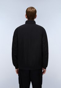 Giubbotto bomber nero con colletto alto, realizzato in un tessuto liscio. Presenta polsini e orlo a costine, con un design minimalistico privo di motivi.