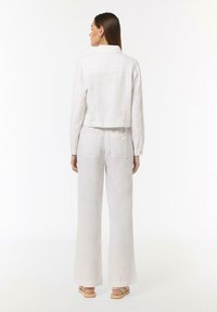 Lekka, biała, lniana kurtka w fasonie cropped z długimi rękawami i kołnierzem, zestawiona z szerokimi lnianymi spodniami; obie części mają gładką fakturę.