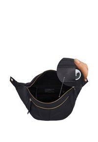 Schwarze Leder-Gürteltasche mit offenem Reißverschluss, die eine Innentasche zeigt, in der ein rundes weißes Gerät von einer Hand gehalten wird, Detailausschnitt.