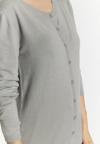 Cardigan grigio a maglia con scollo a V, maniche lunghe e chiusura con bottoni sul davanti, dotato di bottoni coordinati. Texture liscia.