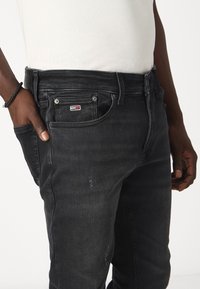 Černé džíny ze džínsoviny s úzkým střihem, klasický pětikapsový design, opotřebované detaily a malá loga na přední kapse.
