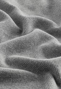 Tissu gris texturé en motif gauffré, exposé en doux plis qui mettent en valeur son drapé et sa structure matérielle.