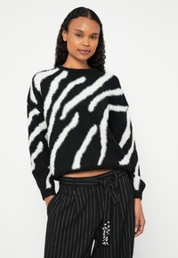 Pull à rayures noires et blanches avec une texture duveteuse, doté d'un col rond et d'une coupe ample. Associé à un pantalon à fines rayures et à des accents décoratifs.