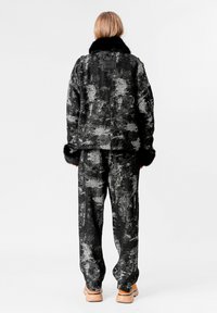 Chaqueta de patrón negro y gris con cuello de piel sintética, pantalones a juego y zapatos de plataforma marrones. Presenta una etiqueta en la parte de atrás.