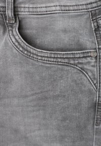 Gros plan sur une poche de jean en denim gris avec des coutures visibles et un petit rivet métallique sur le bord.