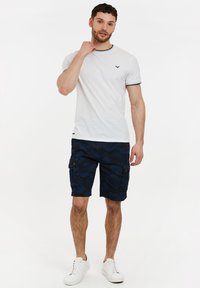 Hvid bomulds T-shirt med marineblå kant, parret med mørkeblå camo cargo shorts med sidelommer og brune knapdetaljer. Hvide sneakers.