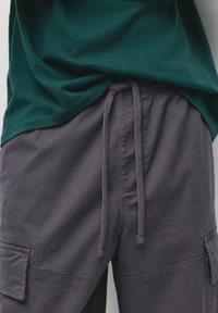 Mørkegrå cargo shorts har et elastisk taljebånd med snor, parret med en grøn kortærmet T-shirt i bomuld.