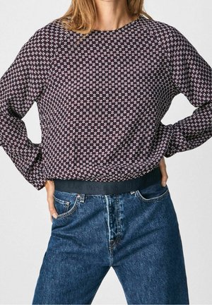 Top de manga larga con un patrón floral en azul marino y blanco, combinado con jeans de tiro alto en azul que tienen una cinturilla negra con logo.