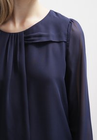 Marinebluse aus leichtem Material, mit plissiertem Ausschnitt und transparenten langen Ärmeln. Glatte Textur mit lockerem Schnitt.