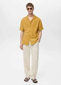 Short-sleeve, mustard-colored button-up shirt made of lightweight fabric, paired with light beige trousers and black sandals.