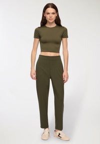 Oliwkowy crop top z krótkim rękawem, zestawiony z oliwkowymi spodniami o wysokim stanie. Model ma na sobie beżowe trampki. Gładka tekstura na całej powierzchni.