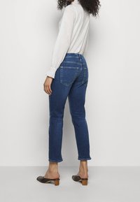 Mörkblå denimjeans med smal passform, uppvikta ankelben och bakfickor, kombinerade med en ljus, långärmad topp och bruna klackmules.