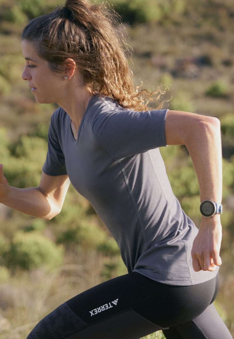 Light gray running shirt with short sleeves, paired with black leggings featuring a textured pattern and white logo. Fitness watch on wrist.