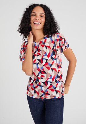 Multikleurige geometrische top van een lichte stof, met korte vlindermouwen en een geplooide halslijn. Gecombineerd met donkere jeans.