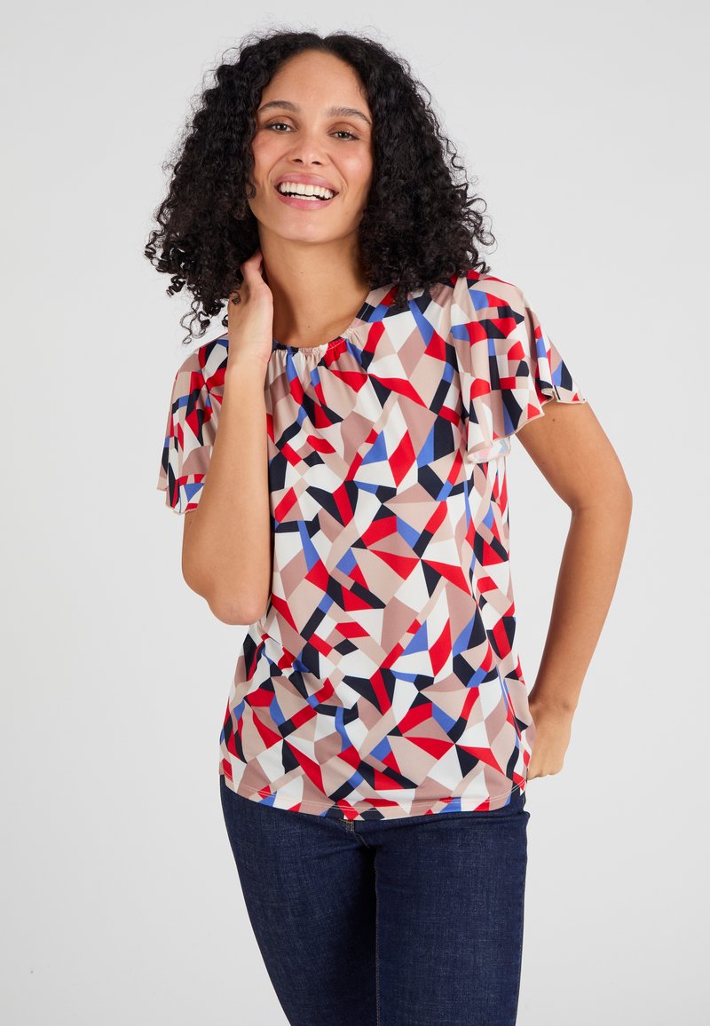 Multikleurige geometrische top van een lichte stof, met korte vlindermouwen en een geplooide halslijn. Gecombineerd met donkere jeans.