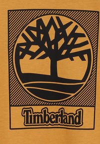 T-shirt di cotone giallo con un grande grafica nera di un albero in design circolare, con accenti a righe e testo "Timberland" sotto.