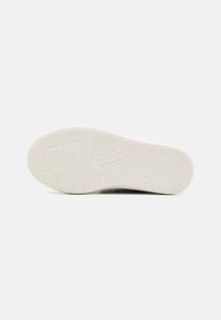Suela de goma blanca con un agarre estampado, superficie texturizada y detalle de logo en relieve. Talón curvado y zona de dedo plano.