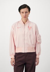 Light pink bomber jacket made of smooth fabric, featuring a zip front, ribbed cuffs, and an embroidered rooster logo with Nike branding.