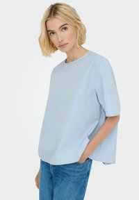 Svetlo modra kratka bluzica s sproščenim krojem, okroglim izrezom in minimalističnim dizajnom. V paru z jeans hlačami, ki poudarjajo preprostost.
