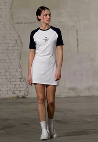 Hvit kort kjole med marineblå raglanermer. Har "tommy girl"-logo på brystet. Modellen har på seg hvite sneakers og sokker. Glatt stofftekstur.