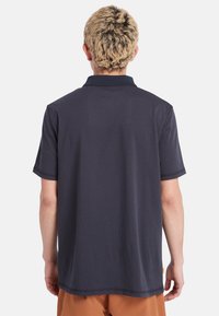 Polo de color marino con mangas cortas, cuello acanalado y detalle en las costuras laterales. La tela parece suave y transpirable. Presenta una pequeña etiqueta con el logo.