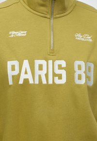 Жълто-зелено суичър с цип и бял надпис "PARIS 89," "Wellness Center Le Marais," и "Stay Cool And Relaxed" на гърдите.