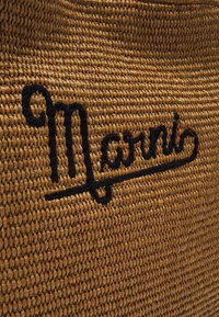 Pleciona torba ze słomy o teksturowanej beżowej powierzchni, zdobiona czarnym haftowanym logo "Marni". Czysty, pleciony design z naturalnym wykończeniem.