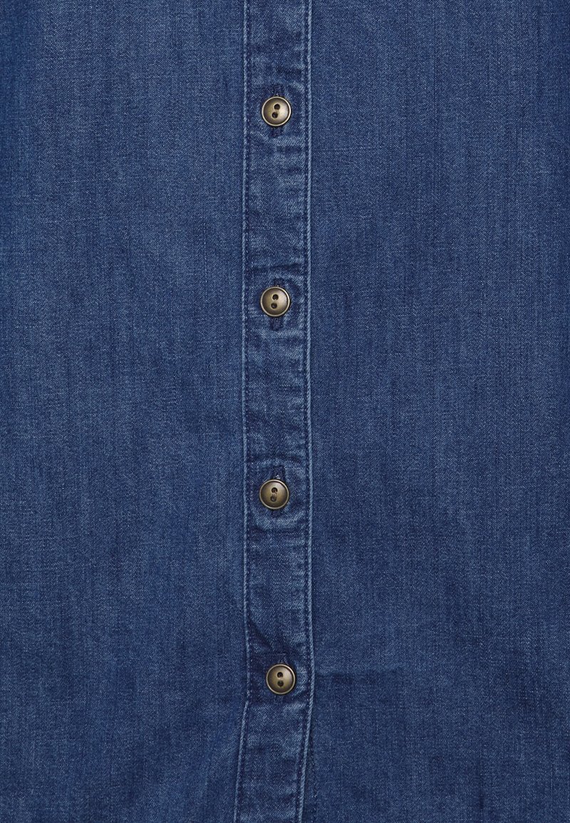 Tessuto di jeans blu scuro con una fila verticale di cinque bottoni marroni lungo una patta dei bottoni rinforzata.
