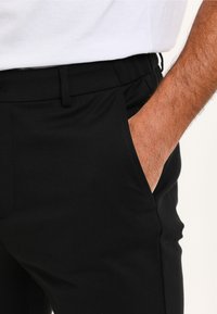 Black pants with a smooth, stretchy texture. Features a side pocket, a flat front, and a waistband with belt loops.