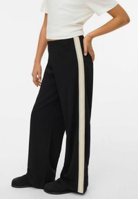 Svarta vida byxor med en krämfärgad sidostripa, med en mjuk textur och elastisk midja. Matchas med en kortärmad vit skjorta.