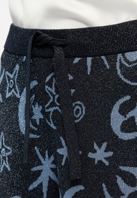 Pantalons à cordon en tricot présentant une base noire avec des motifs célestes bleus. Le tissu a un léger éclat, créant un aspect texturé.