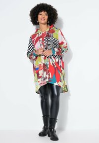 Kleurvolle hoodie-jurk met een mix van rood, groen en ruiten, gecombineerd met zwarte faux leder leggings en zwarte enkellaarsjes.