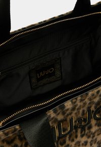 Tote taška s leopardím vzorom, čiernym látkovým interiérom, zlatým zipsom a značkovým logom. Obsahuje vnútornú zipsovú kapsu na uskladnenie.